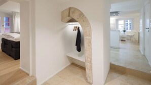 Un interior moderno con un arco de piedra, un banco con ropa y vista a otra habitación con un escritorio y una silla.