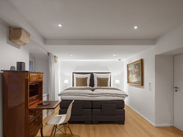 A modern bedroom with a large bed, a wooden dresser, a desk, and a chair.