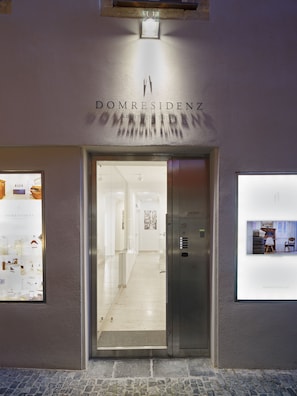 Entrada de hotel con diseño moderno, que presenta una puerta de cristal y un cartel que dice 'DOMRESIDENZ APARTMENT SUITES'.
