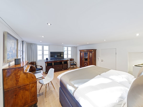 Habitación de hotel con cama, escritorio, silla, televisión, armario y un cuadro en la pared.
