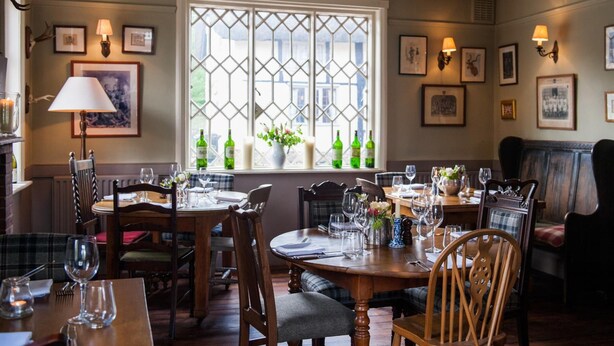 A dining area with a large window, wooden tables, chairs, and wall-mounted lamps. - The Peat Spade Inn (Stockbridge)