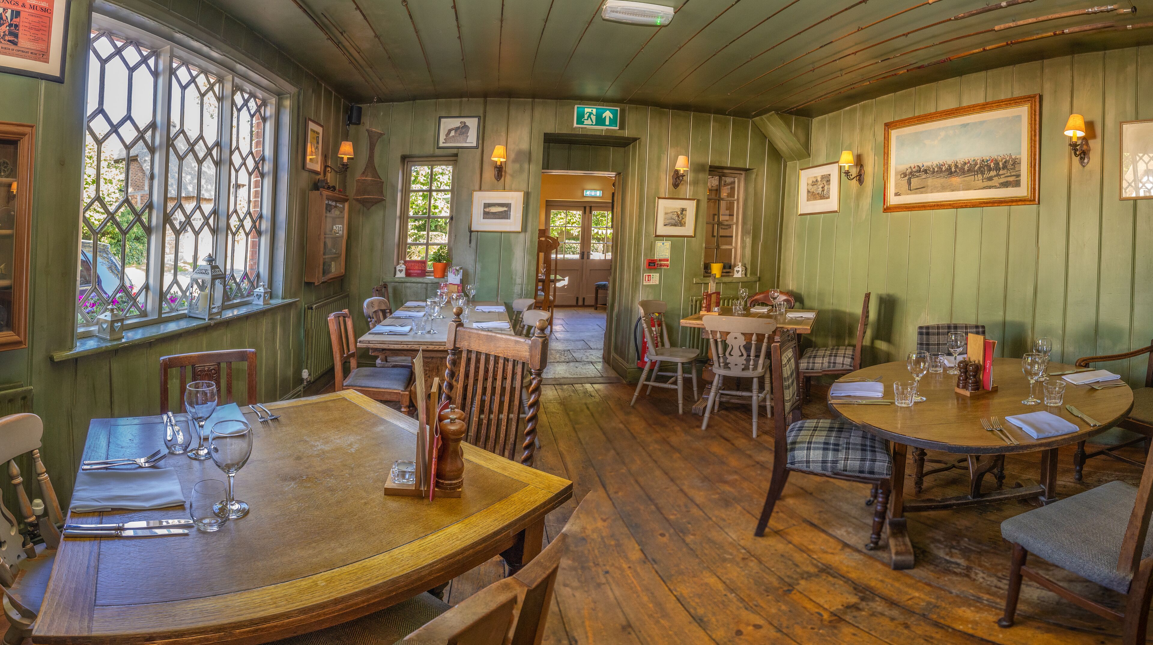 A traditional inn with wooden floors, green walls, and multiple dining tables set with wine glasses and cutlery.