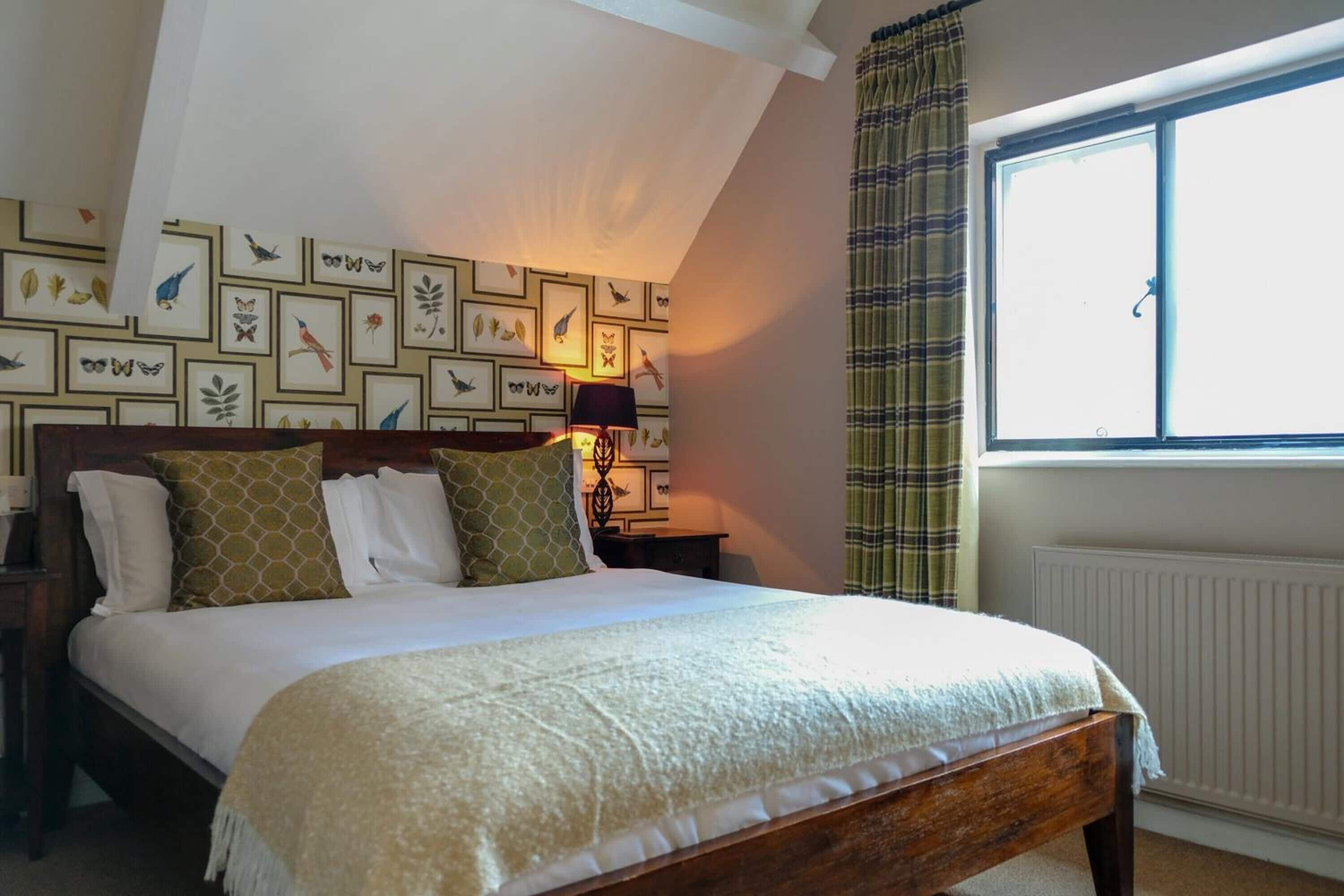 A bedroom with a large bed, a wooden headboard, a wall with framed bird illustrations, a window with curtains, and a radiator.