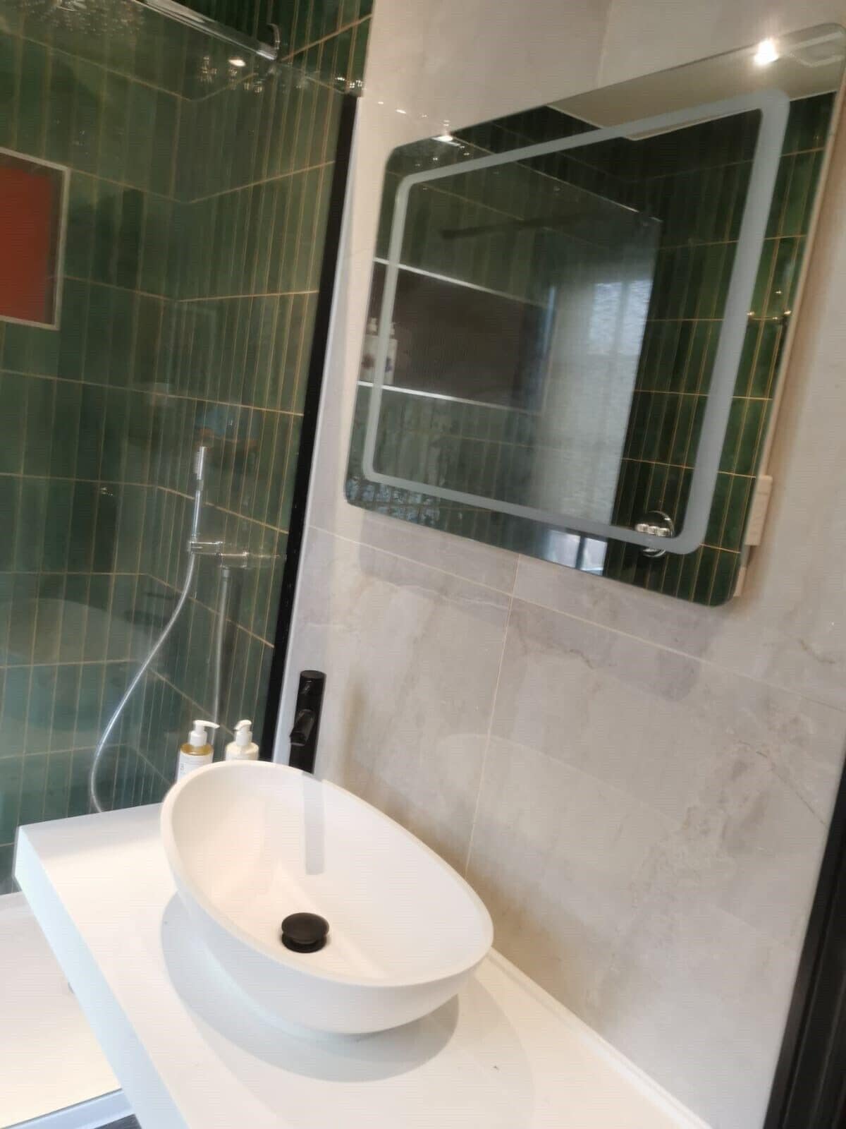 Une salle de bain moderne avec un lavabo blanc, un miroir et des murs recouverts de carreaux verts.