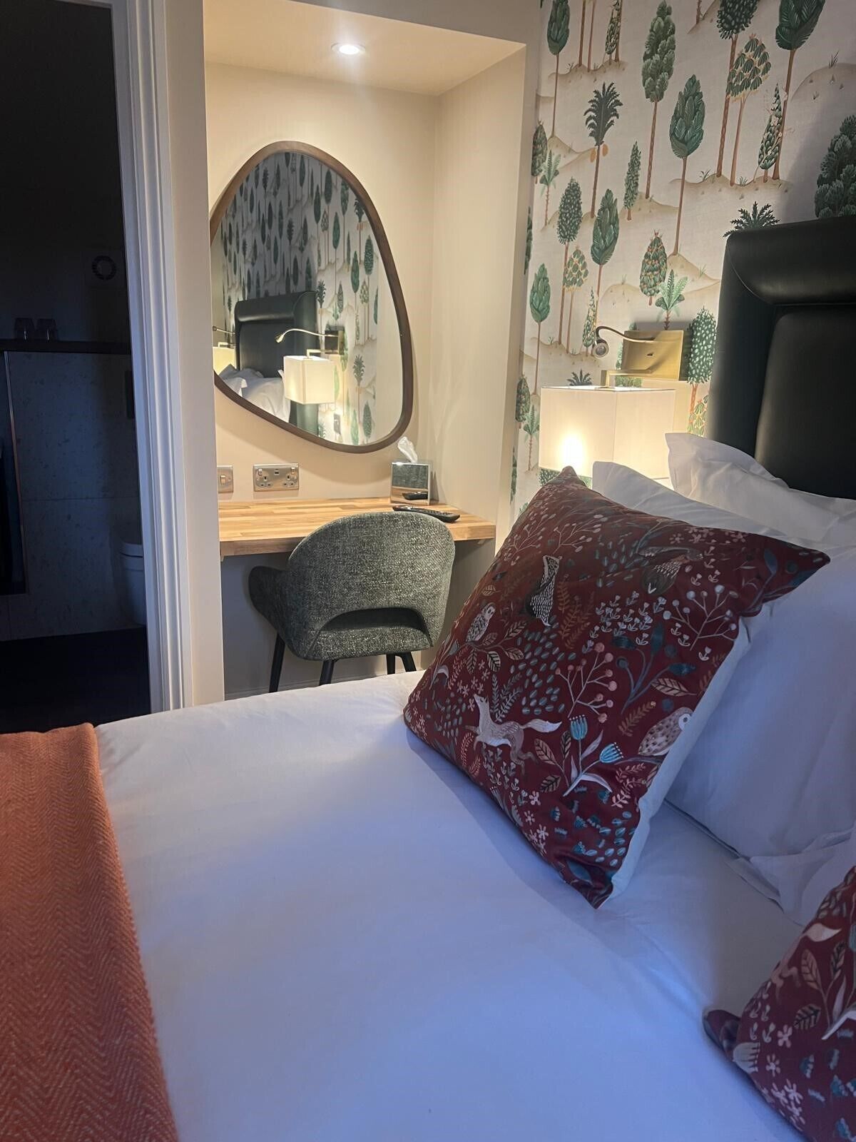 A hotel room with a bed, a desk, a chair, and a mirror.