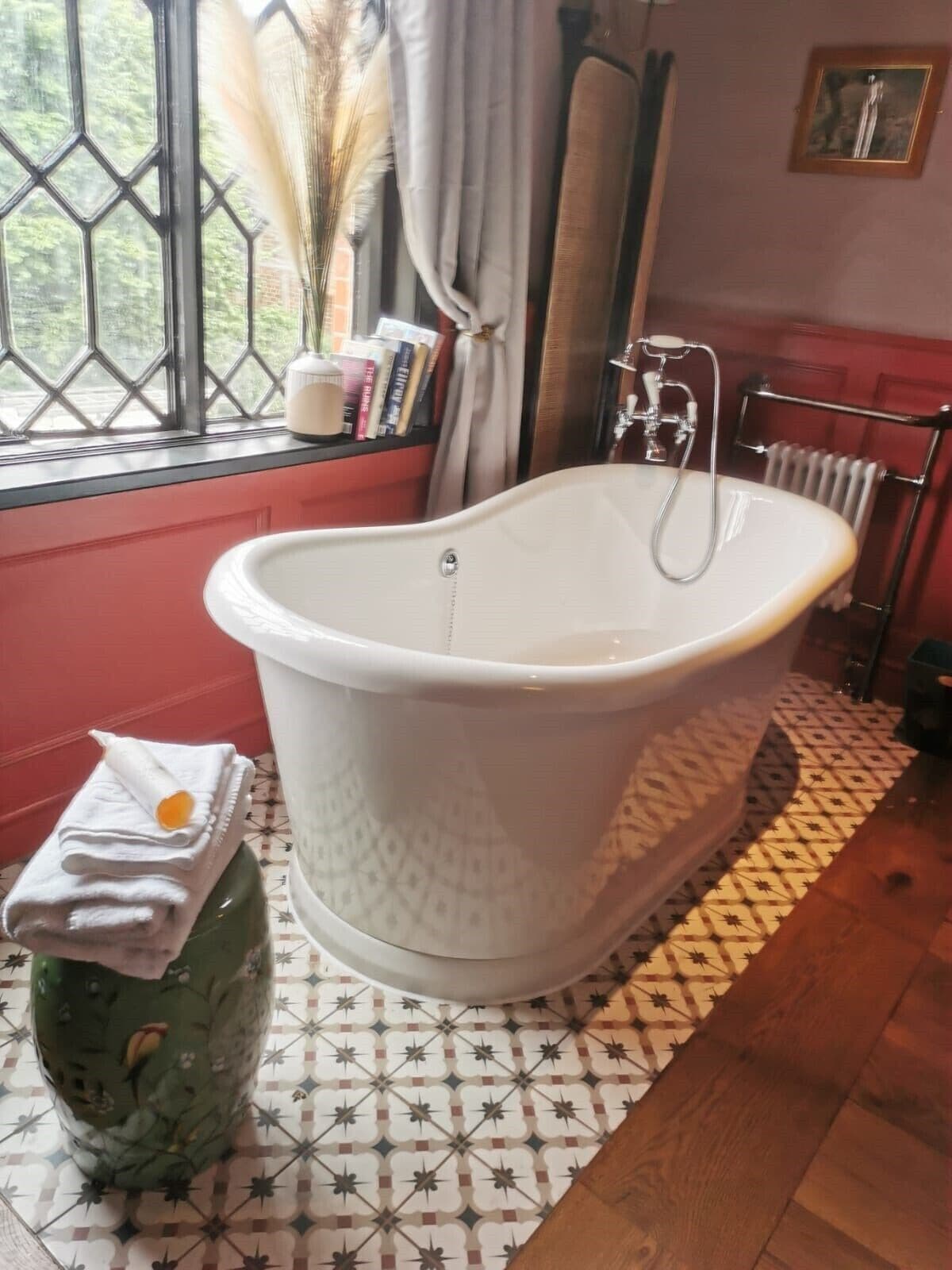 A bathroom with a freestanding bathtub, a radiator, and a window with curtains.