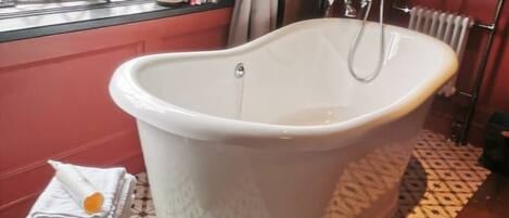A bathroom with a freestanding bathtub, a radiator, and a window with curtains.
