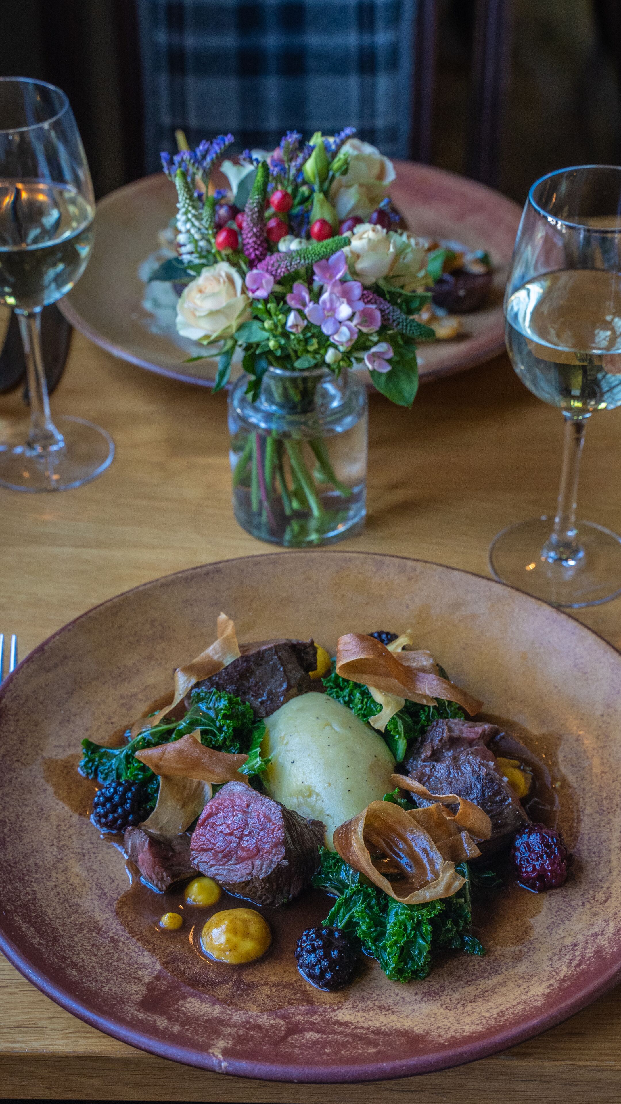 Uma mesa de jantar com pratos de comida, copos de vinho e um vaso de flores.