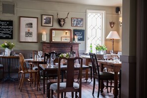 A dining area with wooden furniture, a fireplace, framed pictures, and a wall-mounted deer head.