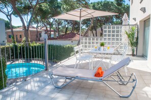 A balcony with a pool, a lounge chair, a table with chairs, and an umbrella. - Apartamentos Porta Coeli  (Castelldefels)