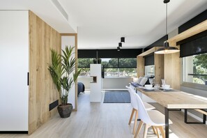 A modern kitchen with a wooden dining table, white chairs, and a large window providing a view of the outdoors. - Apartamentos Porta Coeli  (Castelldefels)