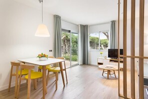 A modern living room with a dining area, large windows, and a TV. - Apartamentos Porta Coeli  (Castelldefels)