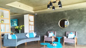A modern living room with a grey sofa, two armchairs, and a coffee table. There is a bookshelf, a mirror, and a round mirror on the wall. - Twin Tides Panglao (Panglao)