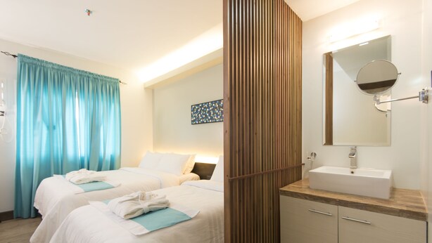 A hotel room with two beds, a bathroom with a sink and mirror, and a wooden panel wall. - Twin Tides Panglao (Panglao)