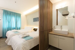A hotel room with two beds, a bathroom with a sink and mirror, and a wooden panel wall. - Twin Tides Panglao (Panglao)