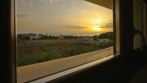 Vista desde una ventana de una puesta de sol sobre un paisaje rural con campos y edificios.
