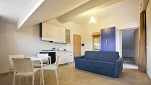 Un espacio habitable compacto con kitchenette, un comedor con sillas blancas y un sofá azul.