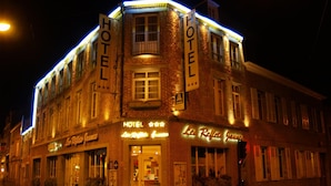 A hotel with a classic brick facade, illuminated signage, and a corner entrance. - Les Reflets Jaunes (Givet)
