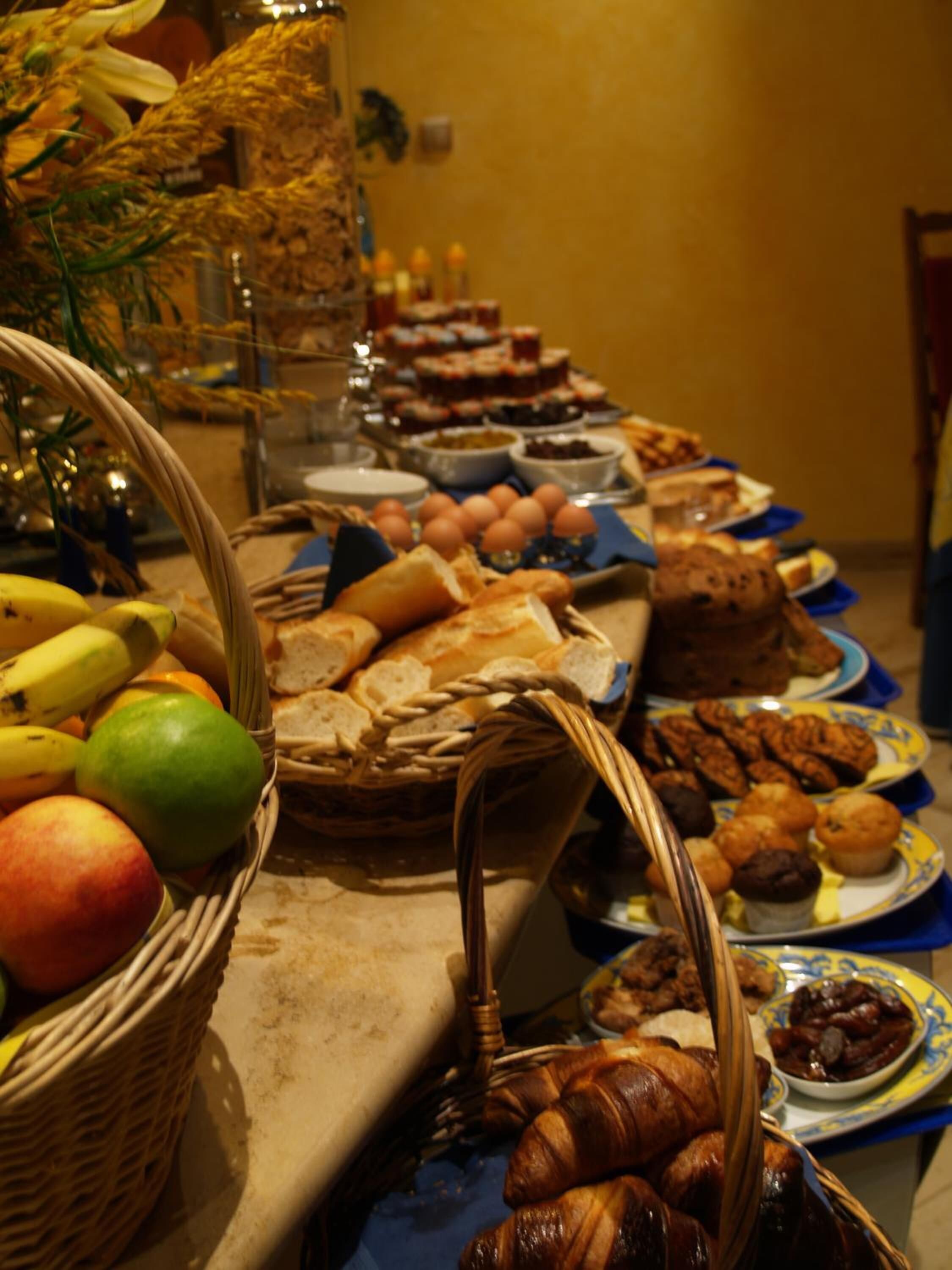 Una mesa de buffet con diversos alimentos, entre ellos frutas, pan, pasteles y postres.