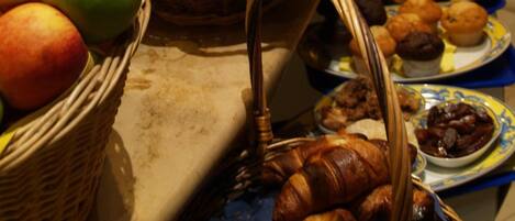 A buffet table with various food items including fruits, bread, pastries, and desserts.