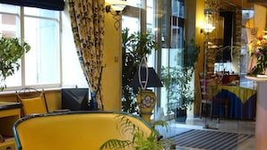 A hotel lobby with a yellow sofa, a glass coffee table with magazines, and a patterned rug. - Les Reflets Jaunes (Givet)