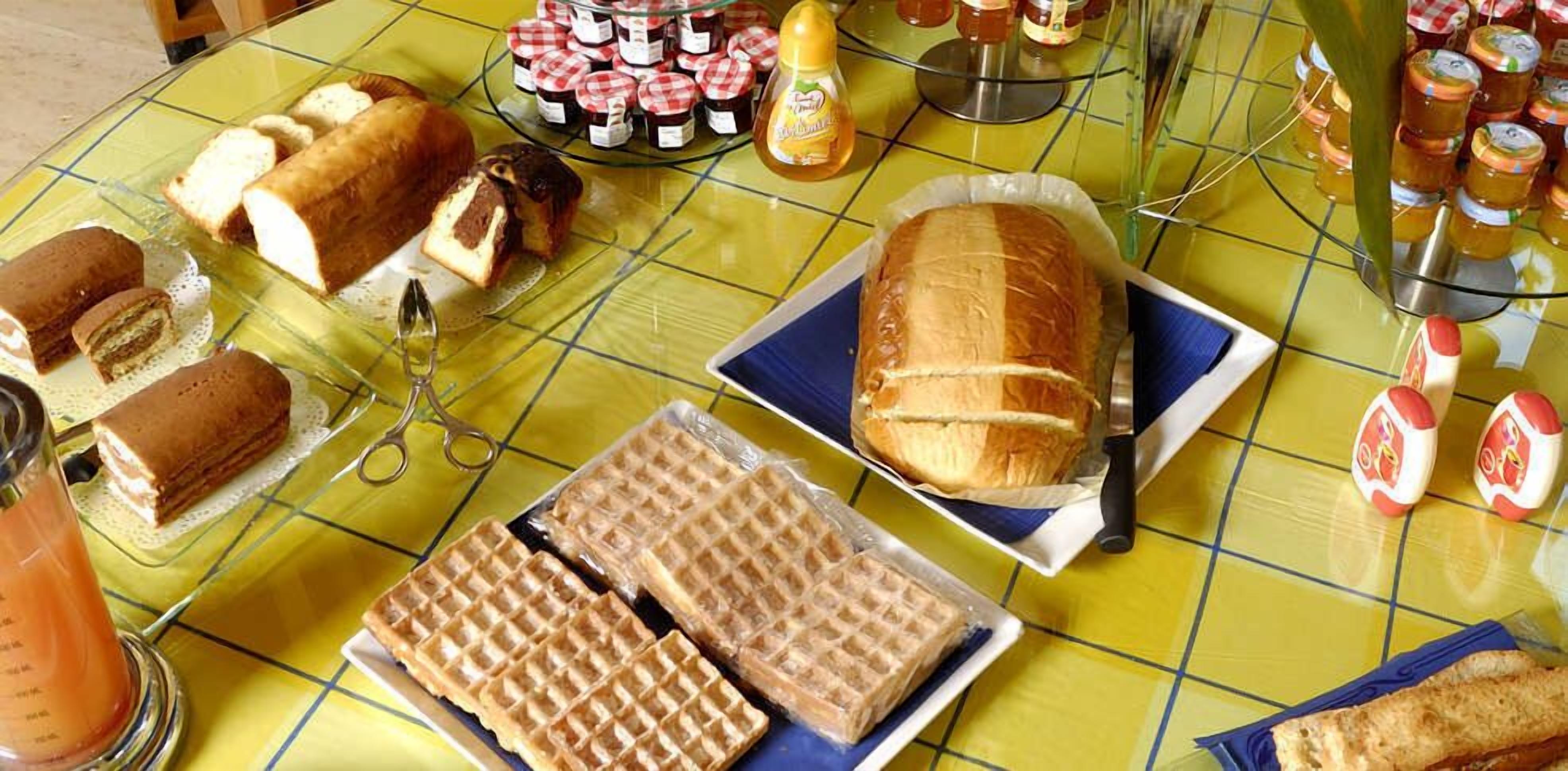 Pöydällä on tarjolla erilaisia leivonnaisia ja jälkiruokia, kuten leipä, sämpylöitä ja lautanen vohveleita.
