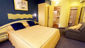 Une chambre d’hôtel avec un grand lit, une chaise, une armoire et une salle de bain visible à travers une porte ouverte.