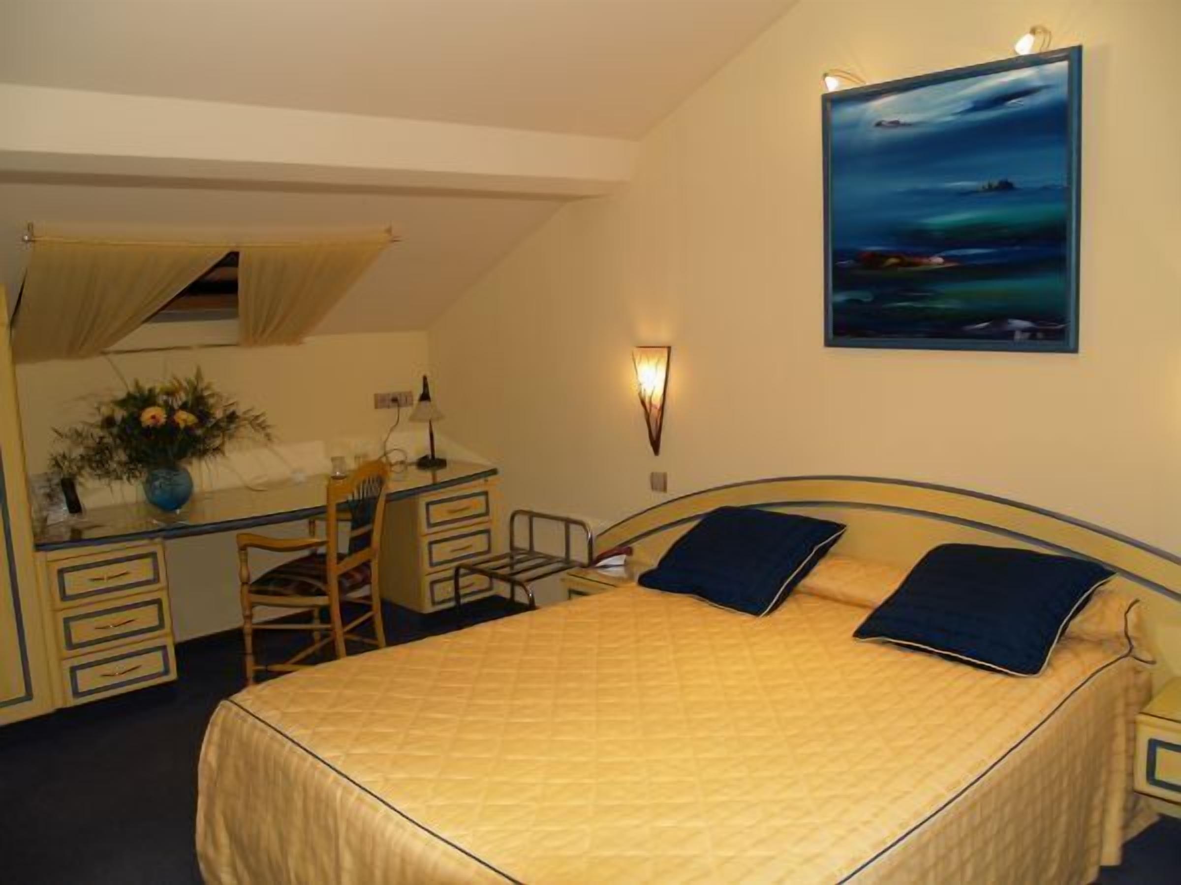 A bedroom with a bed, a desk, a chair, and a painting on the wall.