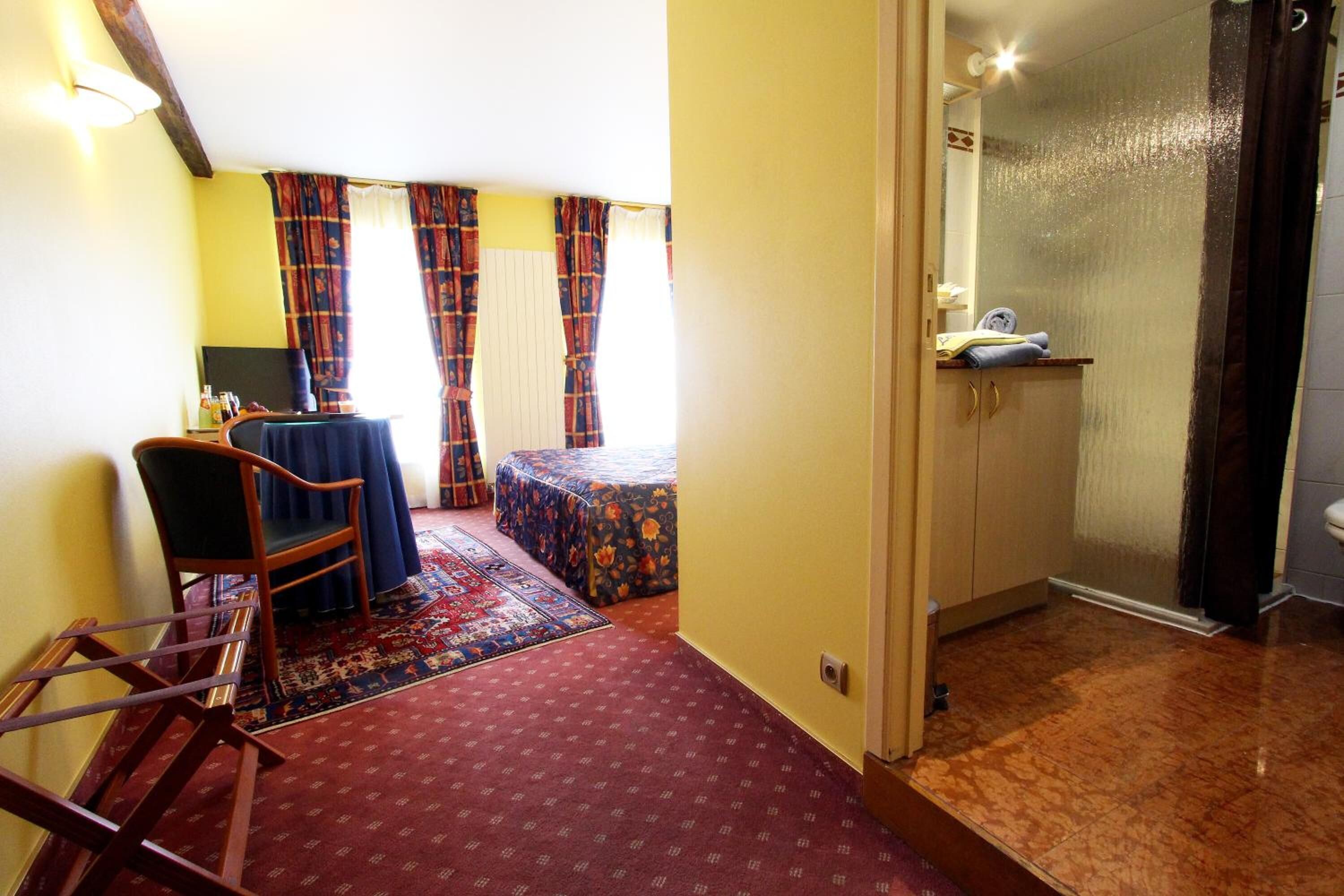 A room with a bed, a chair, a table, and a small bathroom.