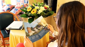 A person reading a book with a laptop on a table, surrounded by a bouquet of flowers. - Les Reflets Jaunes (Givet)