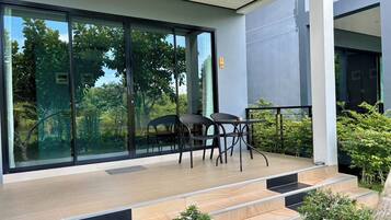 A modern outdoor balcony with a glass wall, a seating area with chairs, and a staircase leading to the entrance.