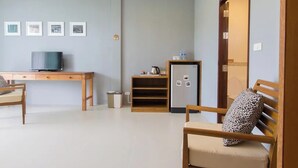 A living room with a wooden desk, a television, a refrigerator, and a sofa with a leopard print cushion. - Moonlight Cottage (Pa Klok)