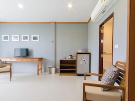 Un salon comprenant un bureau en bois, une télévision, un réfrigérateur et un canapé agrémenté d’un coussin à motifs l éopard.