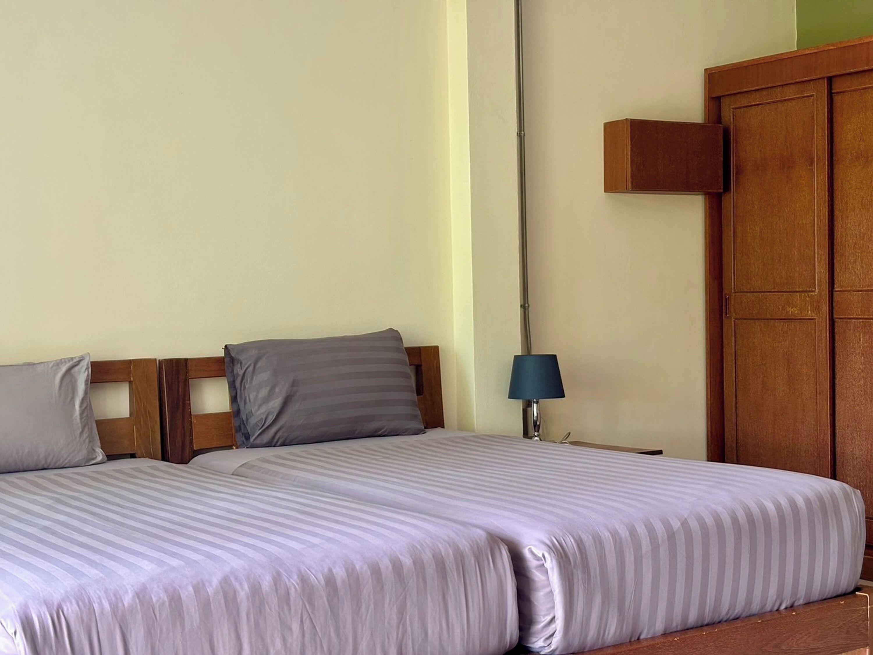 Habitación de hotel con dos camas individuales, una mesita de noche con lámpara y un armario de madera.