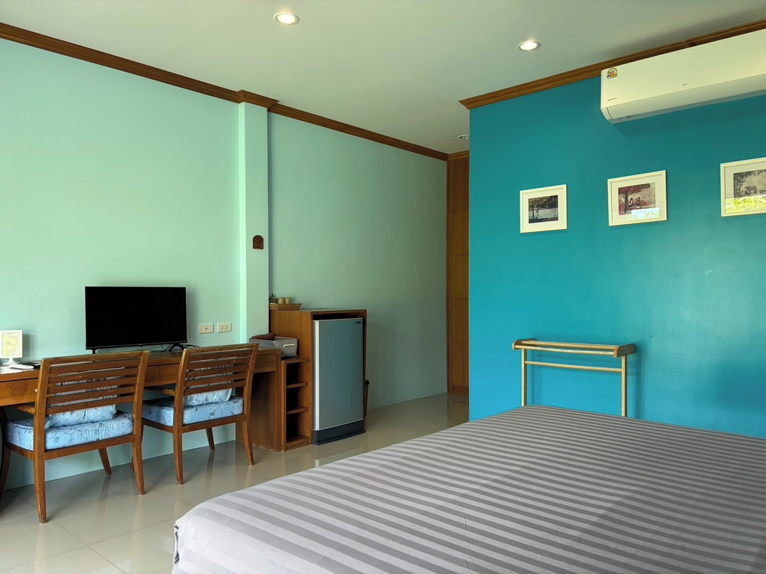 Ein Hotelzimmer mit einem Bett, einem Schreibtisch mit Computer, einem Stuhl, einem kleinen Kühlschrank und einer Wand mit drei gerahmten Bildern.