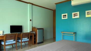Ein Hotelzimmer mit einem Bett, einem Schreibtisch mit Computer, einem Stuhl, einem kleinen Kühlschrank und einer Wand mit drei gerahmten Bildern.