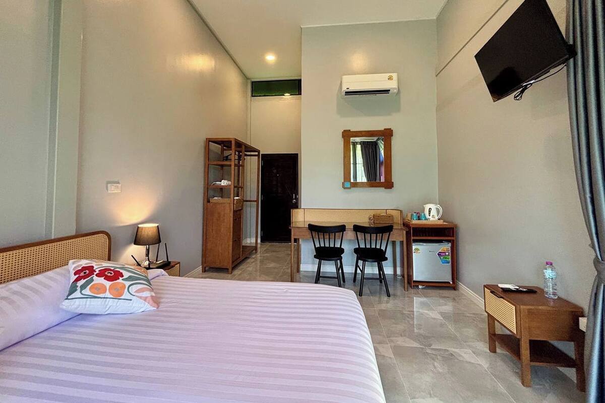 A hotel room with a bed, desk, chairs, a television, an air conditioner, and a wardrobe.
