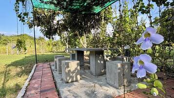 An outdoor seating area with concrete tables and benches under a green canopy.
