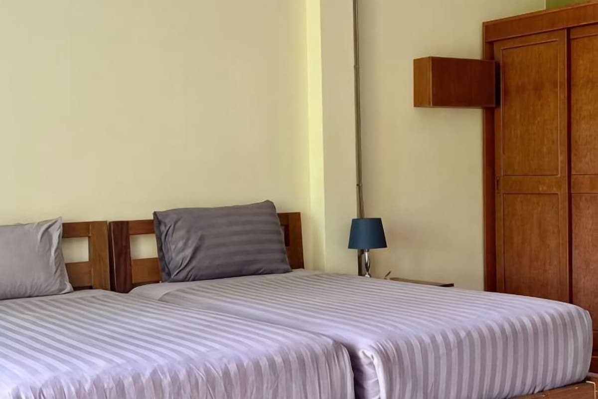 A bedroom with two beds, a wooden wardrobe, and a bedside lamp.