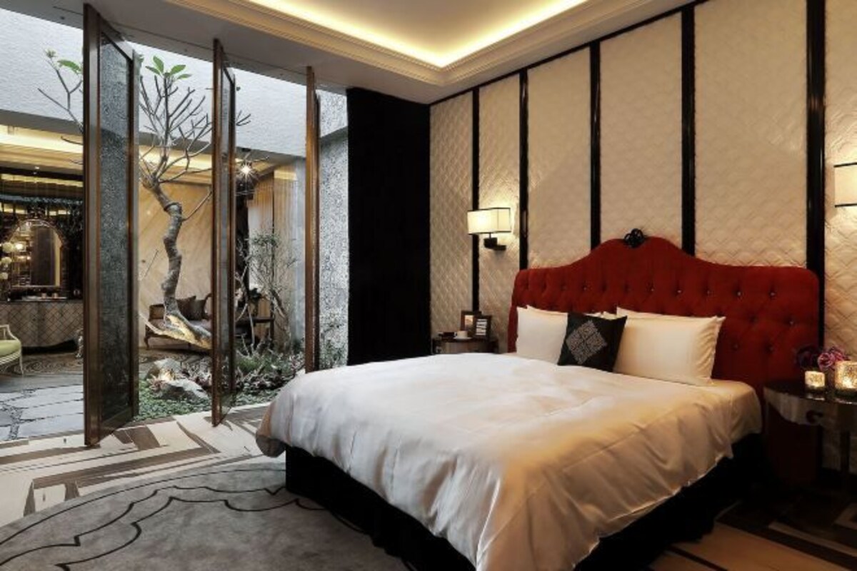 A bedroom with a large bed, a red headboard, a nightstand, and a wall-mounted lamp.