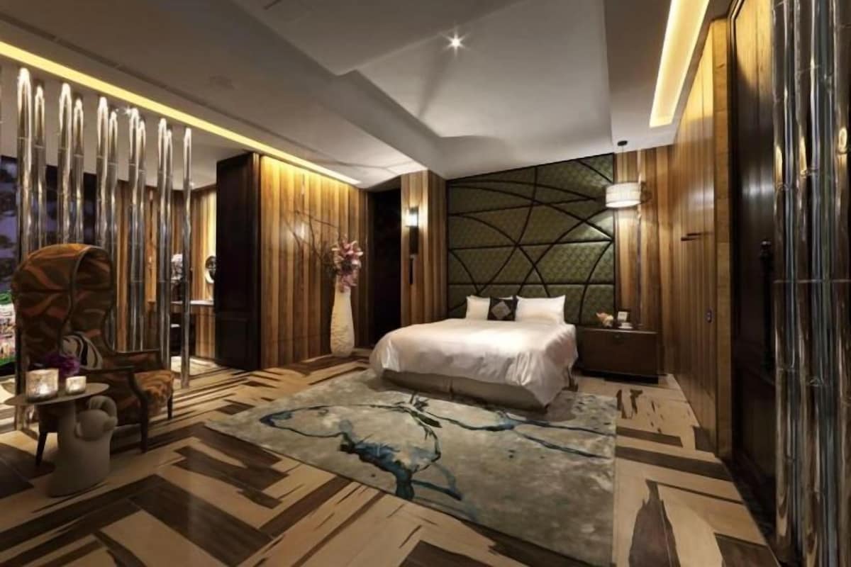 A modern bedroom with a large bed, wooden paneling, and a geometric wall design.