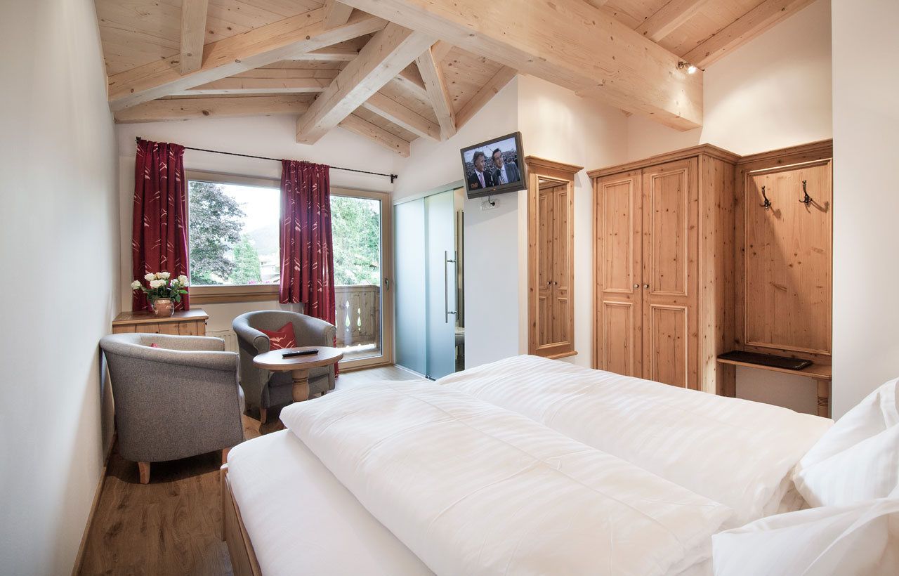 Ein Schlafzimmer mit einem großen Bett, einem Holzschrank, einem an der Wand montierten Fernseher und einem Fenster mit Vorhängen.