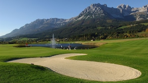 Un parcours de golf avec un bunker de sable, un étang et des montagnes en arrière-plan.