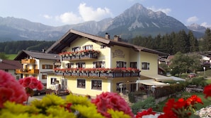Un bâtiment de style alpin traditionnel, doté d’un balcon orné de fleurs, qui se détache sur un paysage de montagnes.