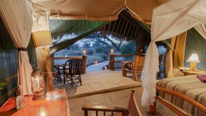 A tented room with a bed, a table with a lamp, and a view of the outdoors. - Kibo Safari Camp (Amboseli)