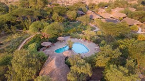 An aerial view of a resort with a central swimming pool, surrounded by thatched-roof huts and lush greenery. - Kibo Safari Camp (Amboseli)