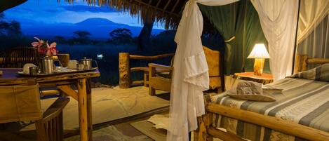 Alojamiento tipo tienda de campaña con una cama, una mesa con lámpara y vistas a una montaña al anochecer.