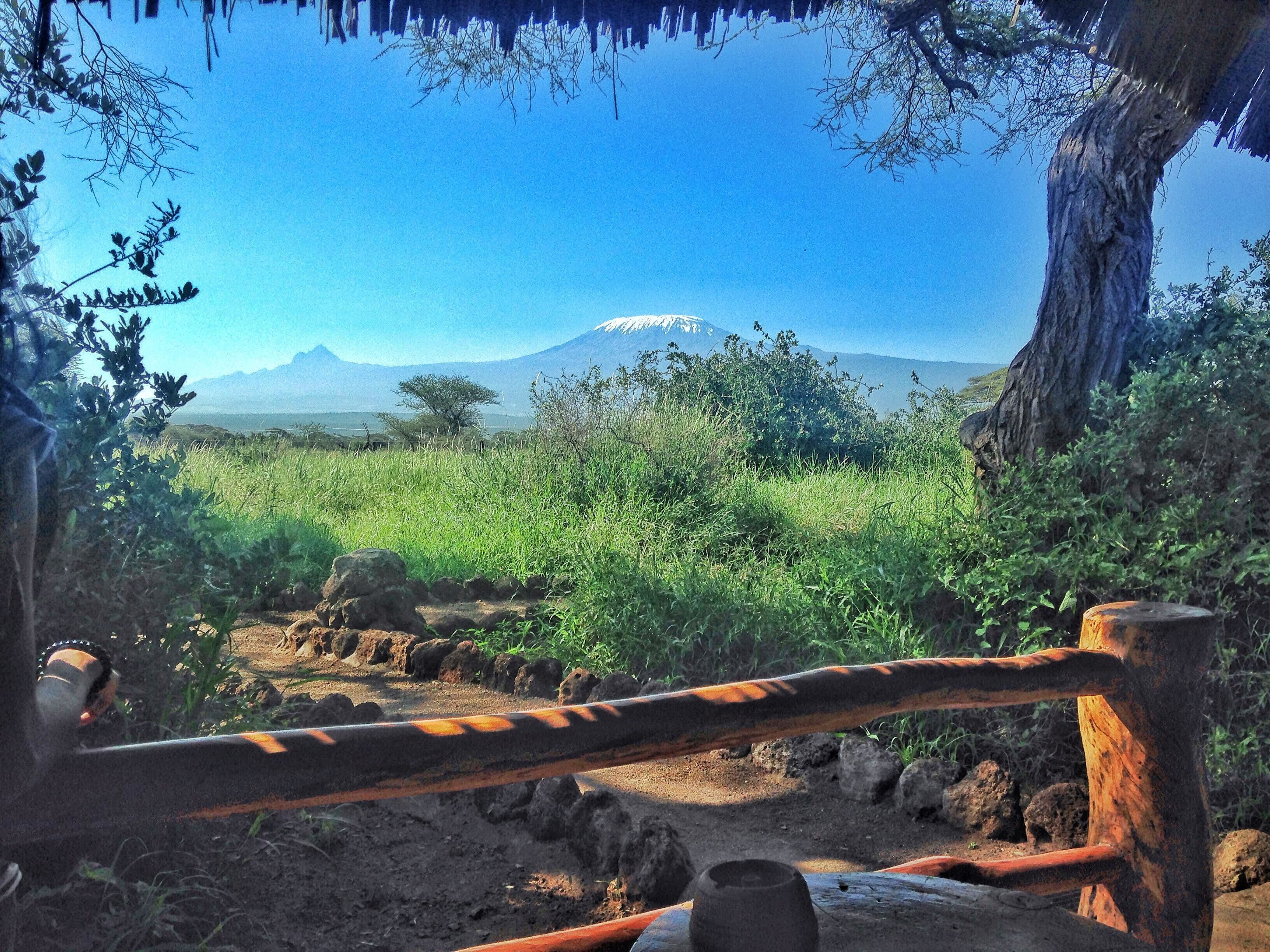 A rustic outdoor setting with a thatched roof structure, a dirt path, and a view of a mountain range.