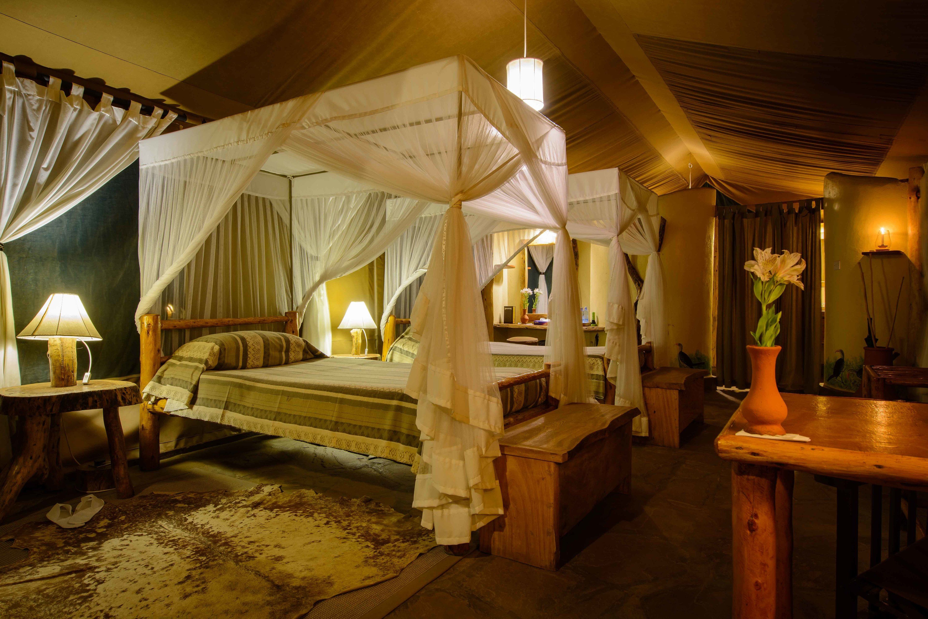 A room with a four-poster bed, wooden furniture, a small table, and a vase with flowers.
