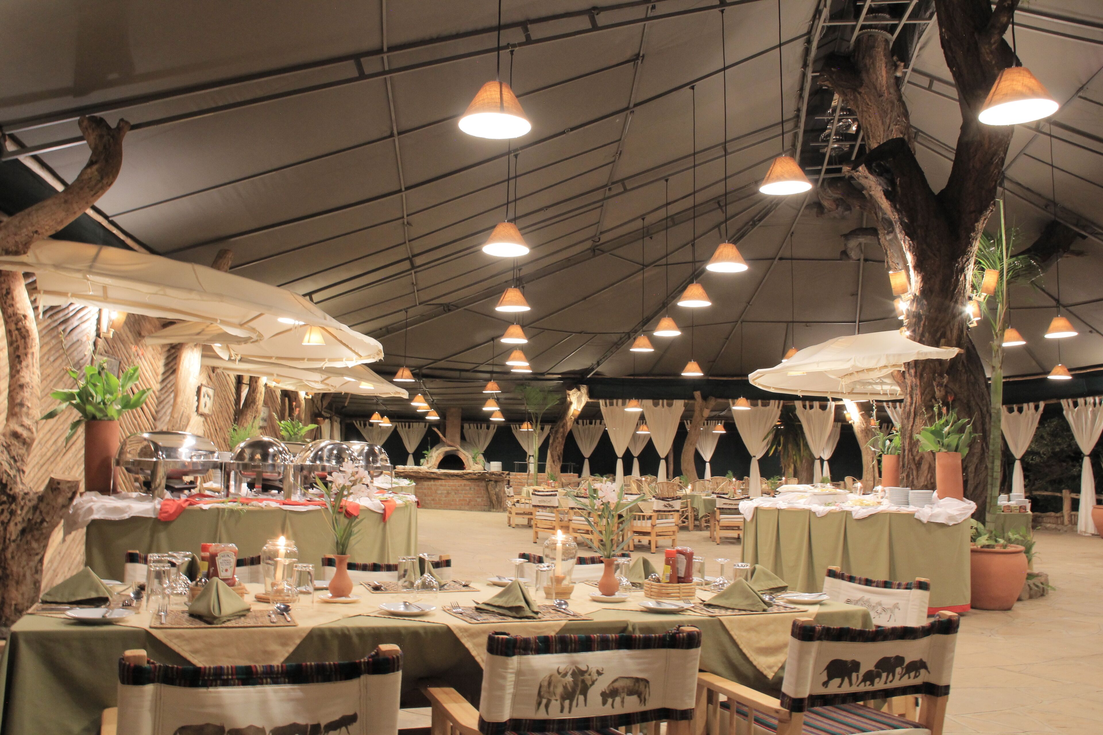 An indoor dining area with tables set for meals, overhead lighting, and potted plants.